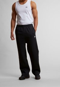 Sorte joggingbukser med elastisk taljebånd og sidelommer, kombineret med en hvid ærmeløs tanktop med et lille logo. Tekstureret stof.