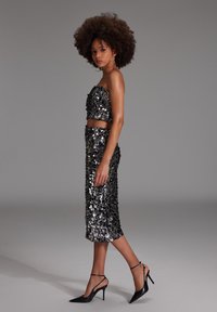 Ensemble deux pièces noir en sequins comprenant un top court sans bretelles et une jupe mi-longue, associé à des escarpins noirs pointus et des boucles d'oreilles créoles.