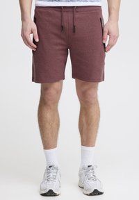 Shorts bordeaux avec une taille à cordon de serrage, et deux poches latérales zippées noires. Fabriqués dans un tissu texturé, se terminant au-dessus du genou.