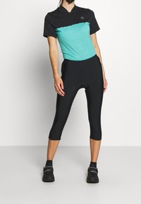 Jersey de ciclismo de manga corta con la parte superior negra y el panel inferior turquesa, combinado con pantalones cortos de ciclismo acolchados negros, que cuentan con cierre de cremallera.
