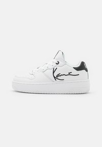 Hvide lædersneakers med en hævet sål, sorte accenter og et karakteristisk signaturdesign på siden. Inkluderer runde snørebånd og perforeringer.