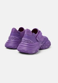 Sneaker viola con suola in gomma texture, retro imbottito e cinturino regolabile. Materiale superiore liscio con design arrotondato e accenti distintivi.