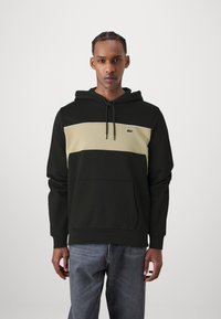 Haut à capuche en mélange de coton noir et beige avec un effet color-block. Il comporte une poche avant, une capuche ajustable et un petit logo sur la poitrine.