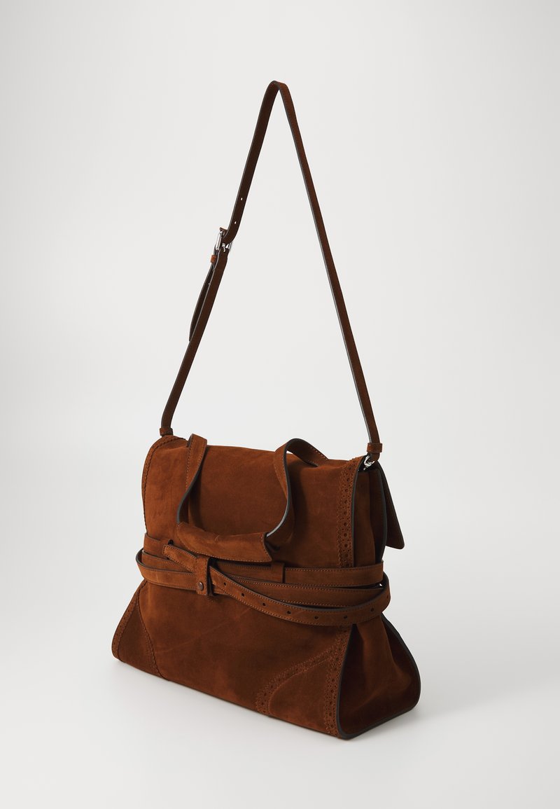 Brun mockaläderhandväska med en strukturerad design, featuring en lång, justerbar rem och dekorativa perforerade detaljer.