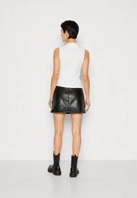White sleeveless top with high collar, paired with a black leather mini skirt. Features a smooth texture and fitted silhouette. Black ankle boots.
