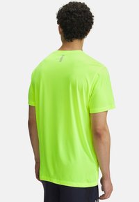Camisa atlética de manga corta en un vibrante color amarillo neón. Presenta un acabado texturizado y un detalle reflectante en el cuello trasero. Material ligero.