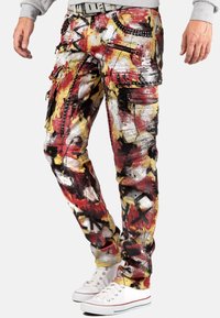 Pantalons cargo multicolores avec un mélange de rouge, de jaune et de noir, ornés de motifs de peinture abstraits, de plusieurs poches, de fermetures éclair et d'accents cloutés.