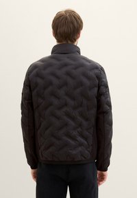 Svart vadderad puffjacka med ståkrage, med en texturerad yta och elastiska cuffs. Enkel design utan synlig utrustning eller dekorationer.