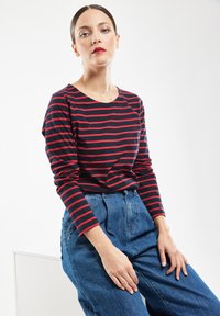 Mørkeblå og rød stribet langærmet skjorte med rund halsudskæring, parret med højtsiddende blå denimbukser. Blødt stof, afslappet pasform.