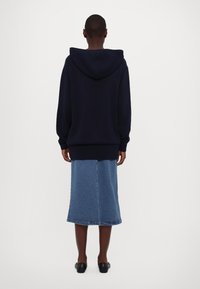 Sweat à capuche bleu marine foncé à coupe ample, avec une grande capuche et des poignets côtelés, associé à une jupe midi en denim bleu clair.