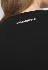 Maglietta nera a maniche corte con scollatura rotonda, caratterizzata da una stampa del logo argento sul retro. Tessuto di cotone liscio con una forma aderente.