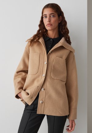 Beige wollen mix jas met een kraag, twee voorzakken en knoopsluiting. Beschikt over gestructureerde stof en zichtbare stikseldetails.