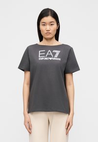 Szara koszulka z krótkim rękawem z fakturowanym srebrnym logo "EA7 EMPORIO ARMANI" na przodzie. Wykonana z miękkiego bawełnianego materiału.