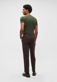 Calças justas castanho-escuro combinadas com um top justo de manga curta em verde-oliva. Apresentam uma textura lisa e uma silhueta aerodinâmica.