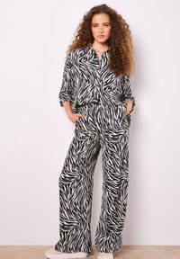 Schwarz-weißes Zebra-Print-Hemd und weite Hosen aus leichtem Stoff. Das Hemd hat eine lockere Passform mit einer knopfbaren Gestaltung.