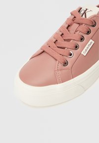 Light pink synthetic sneaker with rounded toe, white rubber sole, metal eyelets, and matching laces; features Calvin Klein logo on side.