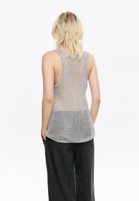 Pilkas mezginis tank top'as su laisvai austų tekstūra. Yra dekoltė ribotas apvadas ir plati iškirpė, demonstruojanti atvirą nugaros dizainą.