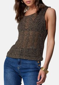 Top in maglia marrone metallizzato con motivo geometrico, dotato di scollo a barca e texture semi-trasparente. Abbinato a jeans blu.