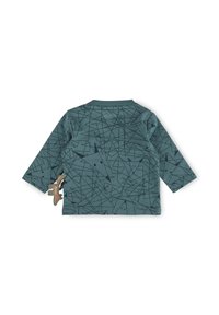 Langärmliges grünes Hemd mit schwarzen geometrischen Mustern und einem kleinen tierförmigen Zubehör, das an der Seite befestigt ist. Weicher Stoff.