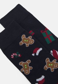 Marineblaue Socken mit bunten Mustern von Lebkuchenmännern, Weihnachtsmützen und Zuckerstangen. Hergestellt aus weichem, gestricktem Stoff.