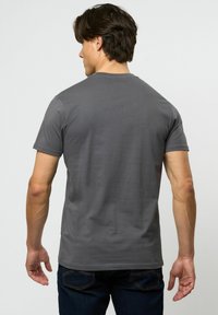 Grå kortermet T-skjorte med rund hals, myk tekstur og tettsittende design, vist på en person fra baksiden, kombinert med mørke jeans.