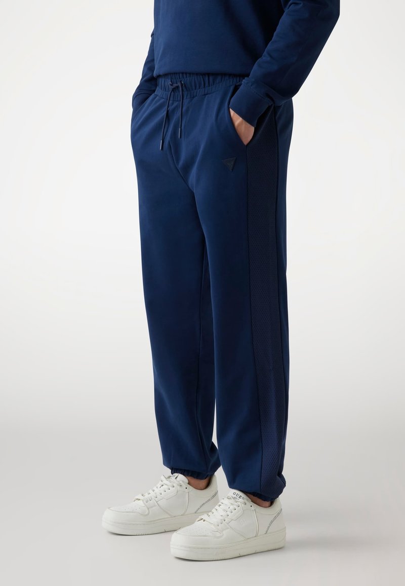 Marineblauwe sweatpants van zacht materiaal, met een elastische tailleband, zijzakken en een contrasterend gaaspaneel langs de buitennaad.