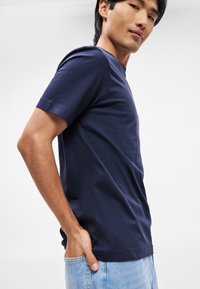 Σκούρο μπλε κοντομάνικο μπλουζάκι από βαμβάκι, με στρογγυλή λαιμόκοψη και λεπτομέρειες στις πλαϊνές ραφές, φορεμένο με ανοιχτό μπλε τζιν. 