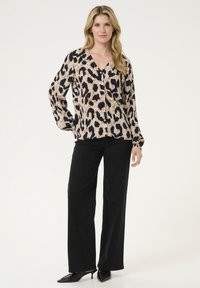 Blouse à manches longues en imprimé léopard beige et noir, avec un col en V, des boutons sur le devant et une coupe décontractée. Associée à un pantalon noir à jambes larges.