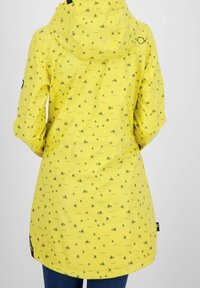 Gul regnfrakke med hætte, der har et gentaget mønster af små både og bølger, lavet af et glat, vandafvisende materiale.