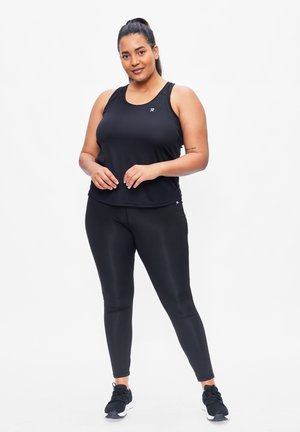 Zwarte sporttanktop met ronde hals, gecombineerd met zwarte strakke leggings. Model draagt zwarte sportschoenen. Glad, lichtgewicht materiaal.