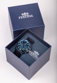 Festina laikrodis mėlynose pakuotėse. Yra mėlynas ciferblatas su sidabrinėmis detalėmis, trys chronografo sub-ciferblatai ir juodas silikoninis dirželis. Dėžutė yra tamsiai mėlyna.
