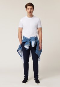 White t-shirt with blue trim, blue denim shirt tied around waist, dark navy pants, and black shoes. Simple and casual attire.