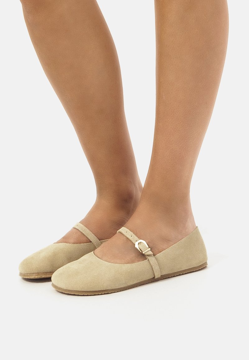 Las bailarina de ante beige presentan una puntera redonda, una correa al estilo Mary Jane con hebilla y una suela de goma natural texturizada.