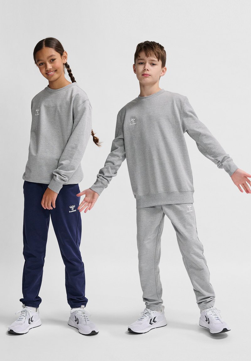 Due due bambini indossano abbigliamento casual: una felpa grigia e pantaloni jogger grigi a destra, e una felpa grigia con pantaloni jogger blu navy a sinistra.