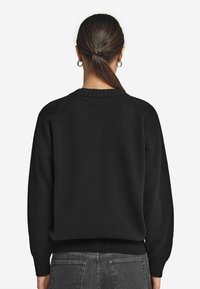 Czarny sweter z okrągłym dekoltem, o luźnym kroju, pleciony z teksturą, z prążkowanymi mankietami i dołem, o prostym fasonie bez widocznych wzorów czy elementów ozdobnych.