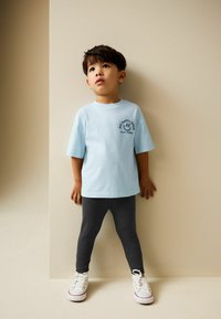 Svetlomodré bavlnené tričko s krátkymi rukávmi, s čiernym grafickým úsmevom; kombinované s tmavosivými rebrovanými legínami a bielymi teniskami.