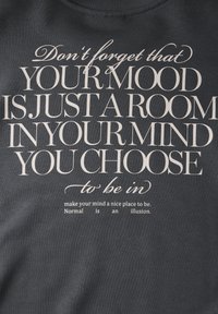Sudadera gris oscuro con texto blanco. El texto incluye una cita motivacional y se presenta en varios estilos tipográficos.