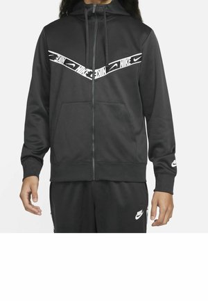 Sweat à capuche noir Nike zippé avec un logo chevron blanc sur la poitrine, associé à un pantalon Nike noir assorti avec un logo blanc sur la cuisse gauche.