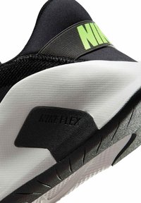 Chaussure de sport noire avec une tige texturée, un logo vert vif et une semelle extérieure blanche épaisse avec des accents noirs et un motif de rainures flexibles.