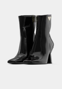 Stivaletti alla caviglia in pelle verniciata nera con punta affusolata e tacco angolare e chunky. Presentano una zip sul lato e un dettaglio metallico con logo.