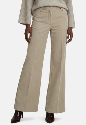 Pantalon large en velours côtelé beige porté avec un pull côtelé beige clair et des bottines à talons hauts pointues marron foncé.