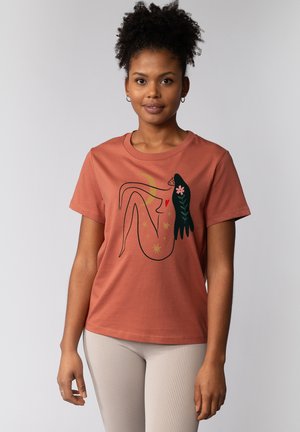 Katoenen t-shirt in roestkleur met een grafische print van een liggende figuur omringd door bloemen en sterren, ronde halslijn en korte mouwen.