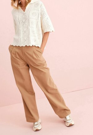 Haut en crochet blanc à manches courtes, associé à un pantalon large couleur beige et des baskets claires. Le haut présente un ourlet festonné et des motifs ajourés.