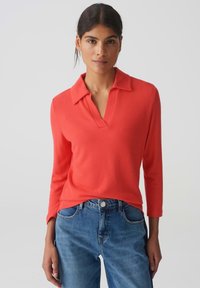 Koraalrode pullover met een kraag en een V-halslijn. Lange mouwen, zachte textuur, gecombineerd met lichtblauwe denim jeans. Eenvoudig ontwerp.