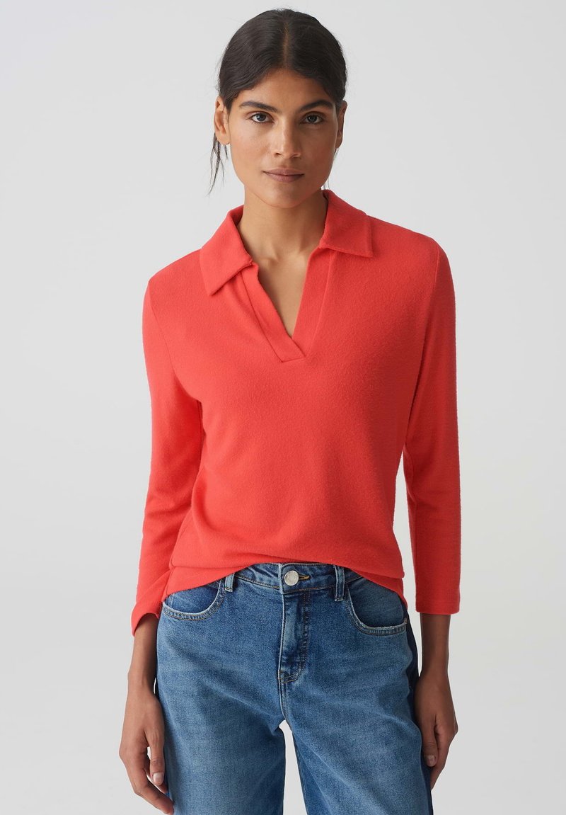 Koraalrode pullover met een kraag en een V-halslijn. Lange mouwen, zachte textuur, gecombineerd met lichtblauwe denim jeans. Eenvoudig ontwerp.