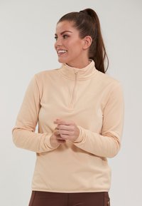 Lys fersken farvet pullover med halvlukket krave, struktureret stof, lange ærmer og en afslappet pasform. Diskret branding nær kraven.