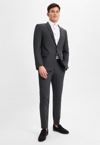 Dunkelgrauer Anzug mit taillierter Passform, Reverskragen, Ein-Knopf-Verschluss und flachen Hose, kombiniert mit einem weißen Hemd und navyblauen Loafers.