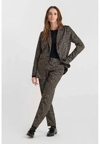 Luipaardprint pak in bruin en zwart, bestaande uit een getailleerde blazer en smalle broek, gedragen met een zwarte top en glanzende zwarte schoenen.