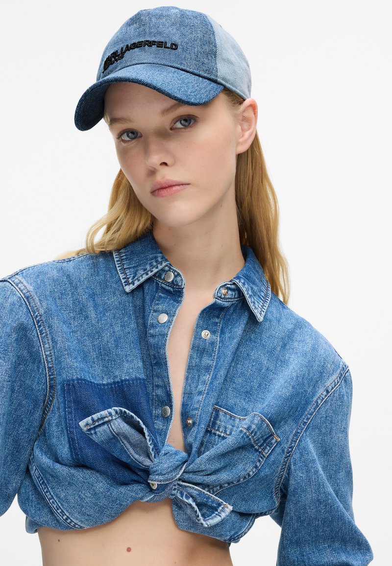 Denims krekls ar mezglu priekšā, ar gaiši un tumši zilu raibumu dizainu. Saskaņots ar zilu denim baseball cepuri.