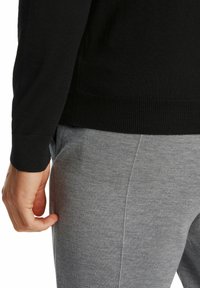 Schwarzer gestrickter Pullover mit gerippten Bündchen, kombiniert mit grauen Jogginghosen, die eine weiche Textur und einen lässigen Schnitt zeigen.